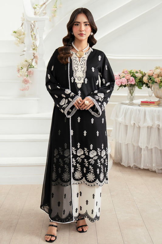 Woman wearing a black and white embroidered traditional outfit in a decorated room.
