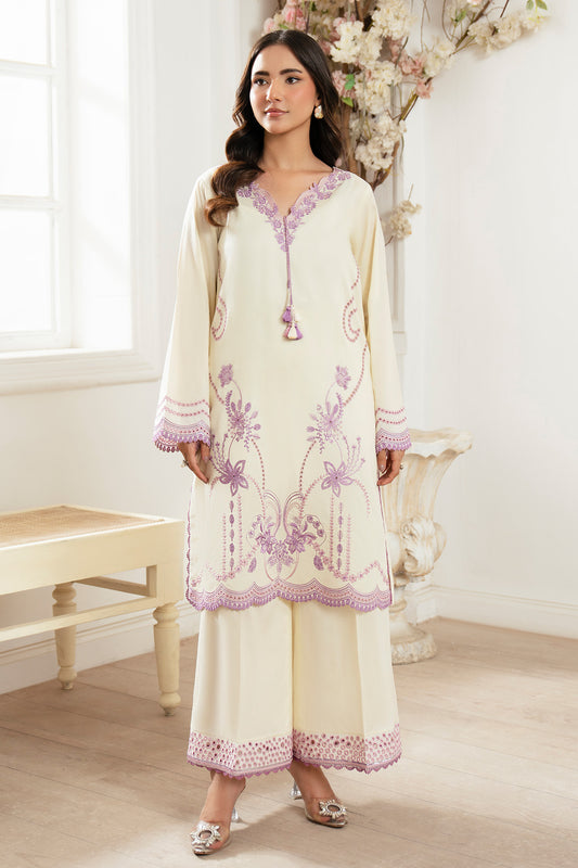 Woman wearing a cream and purple embroidered outfit in a bright room.
