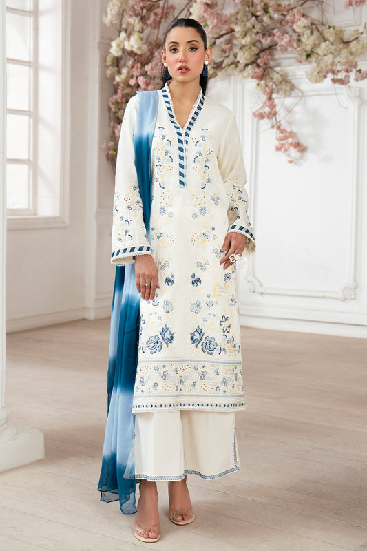 Woman in a white floral dress with blue accents standing in a decorated room.