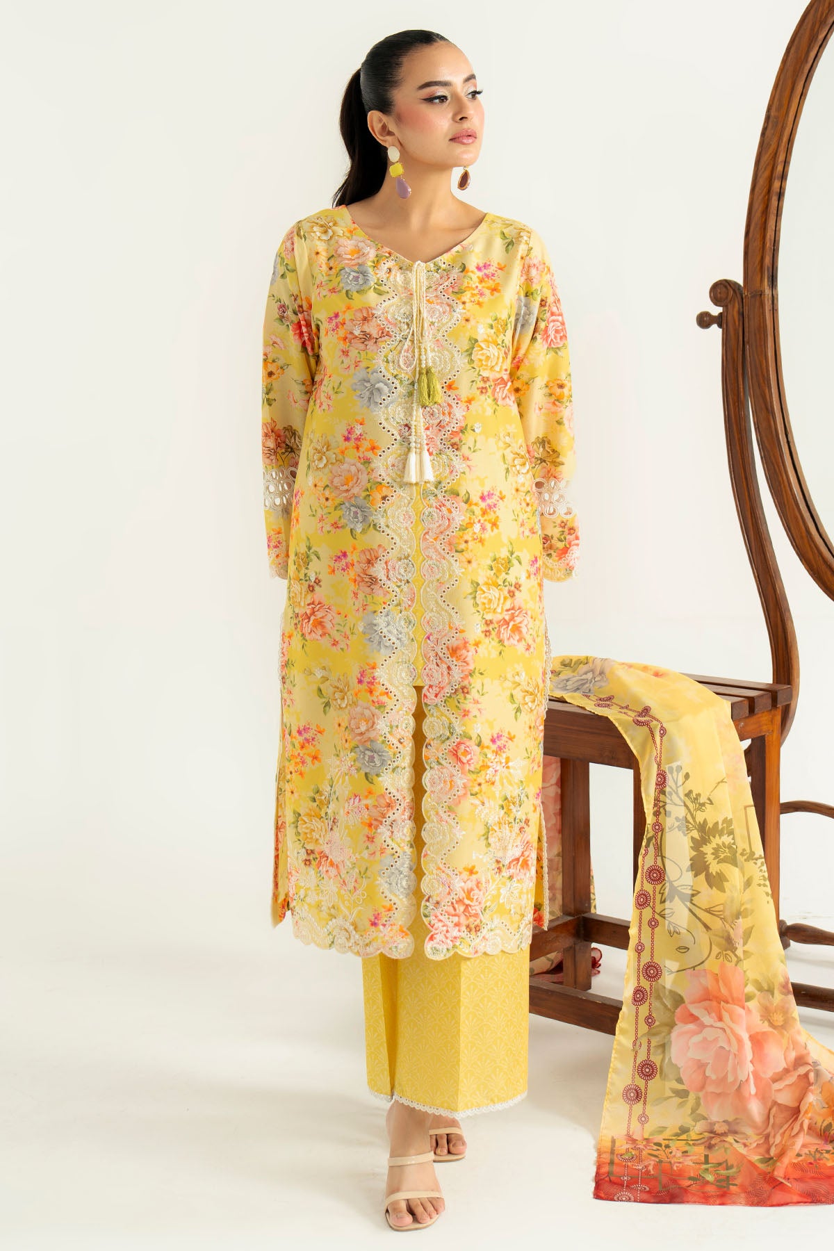 Woman wearing a yellow floral outfit with a matching scarf, standing next to a wooden chair.