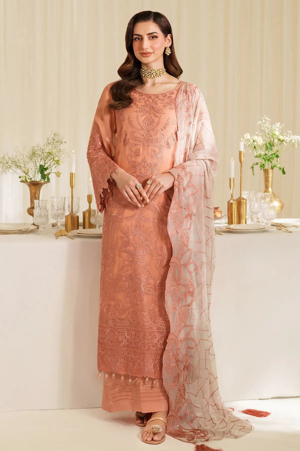 Woman in a peach traditional outfit with a matching dupatta in a decorated indoor setting.