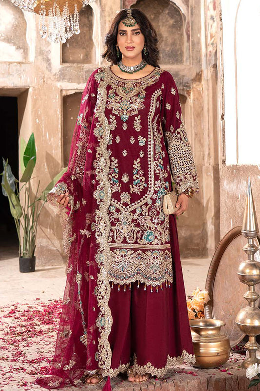 Woman in a maroon embroidered traditional outfit with jewelry in an ornate setting.