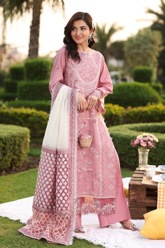 A woman wearing a pink traditional Lawn suit with embroidery and a dupatta, standing outdoors.