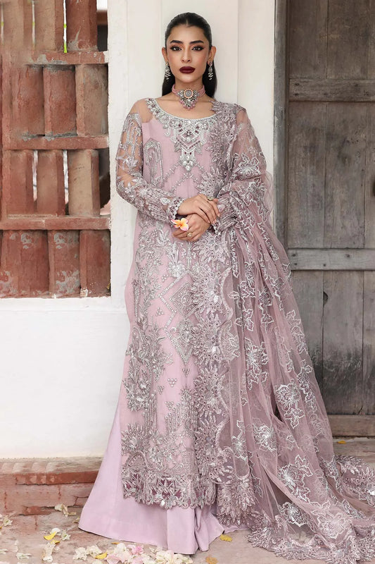 Woman in a pink and silver embroidered traditional outfit standing against a rustic wooden door.