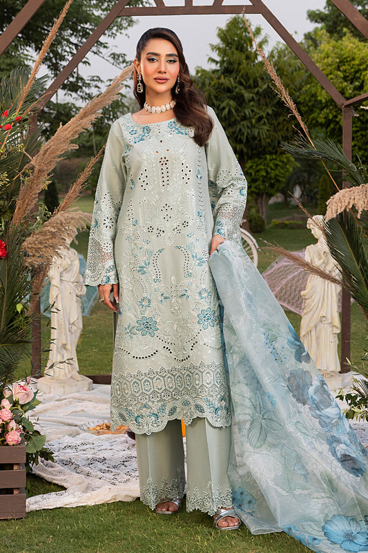 A woman wearing a traditional green dress with intricate embroidery, accompanied by a light blue dupatta with artistic prints, and standing in a garden setting.