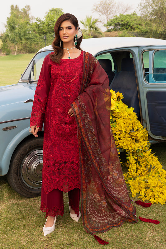 A woman standing beside a vintage car, wearing a red outfit with embroidered cotton shirt, silk dupatta, and matching trousers.