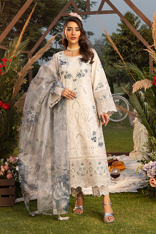 A woman wearing a traditional white dress with blue embroidery, including a shirt, dupatta, and trousers, standing in a garden setting.