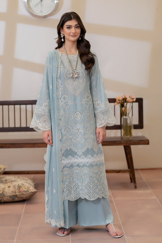 Woman wearing a light blue embroidered traditional outfit in a room with a clock and table in the background.