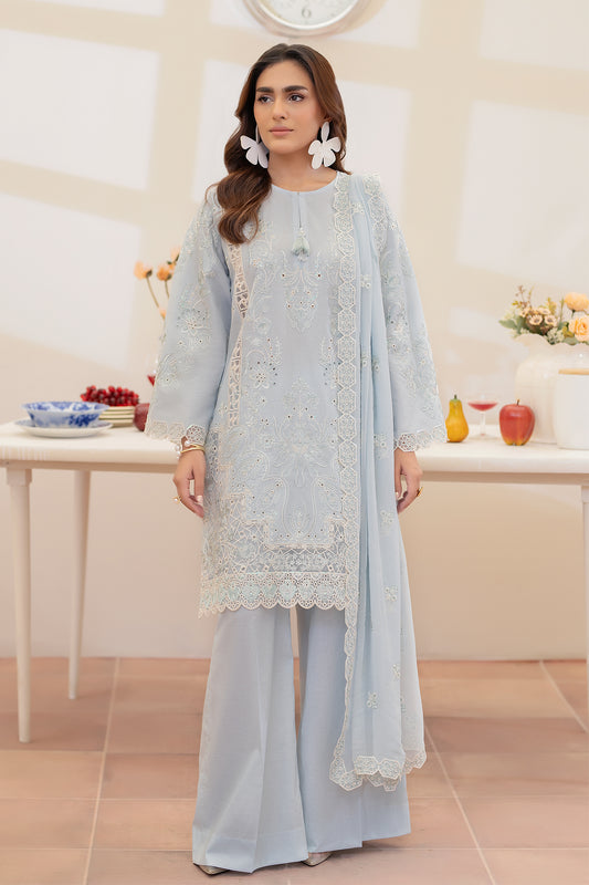 Woman wearing a light blue embroidered outfit in a room with a table and decor.